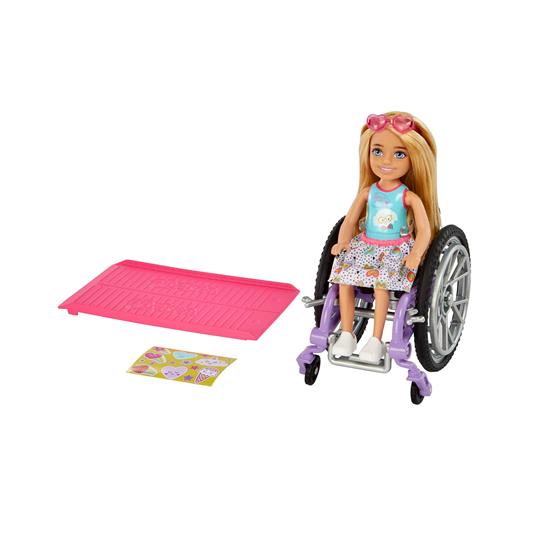 Barbie - Chelsea bambola bionda con sedia a rotelle, che indossa gonna e occhiali da sole, include rampa e foglio adesivi